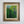 A framed vintage Swedish landscape painting featuring vibrant green trees, presented in a rustic brown wooden frame with a gold inner border, mounted on a light gray wall.