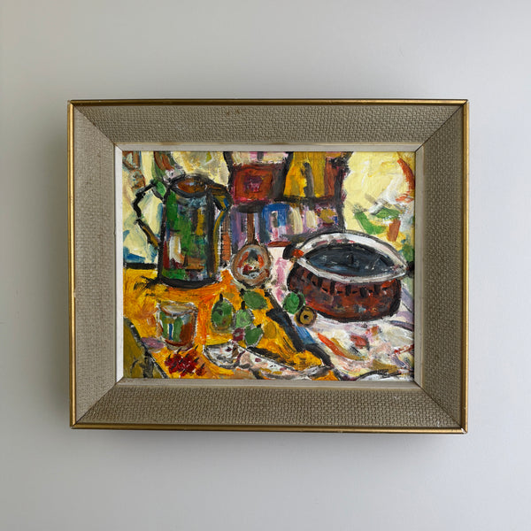 A framed still life mid century oil painting featuring a green coffee pot, a dark cup, and yellow-orange table elements, housed in a textured gold frame against a plain white wall.
