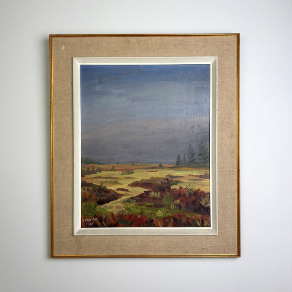 A vintage mid century framed 1964 dated and signed landscape painting on canvas, depicting a moody blue-gray sky over a golden field with dark reddish-brown shrubs in the foreground. The painting is matted with a beige linen mat and enclosed in a gold frame, hanging on a plain white wall.